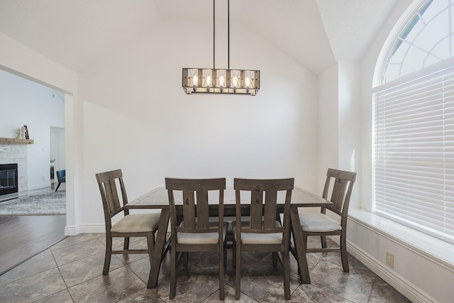 dining space featuring a glass covered fireplace, vaulted ceiling, a chandelier, baseboards, and tile patterned floors