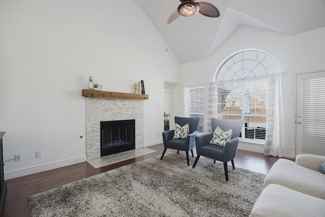 living area with high vaulted ceiling, baseboards, a stone fireplace, and hardwood / wood-style floors