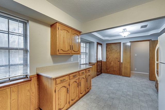 kitchen featuring a raised ceiling, white fridge, a textured ceiling, and wood walls