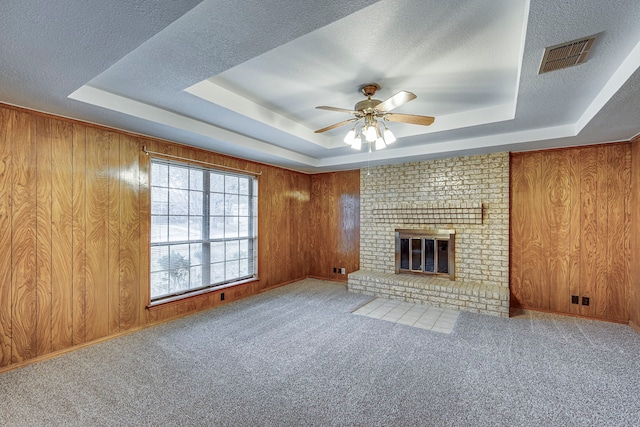 unfurnished living room with a raised ceiling, a brick fireplace, carpet floors, and wooden walls