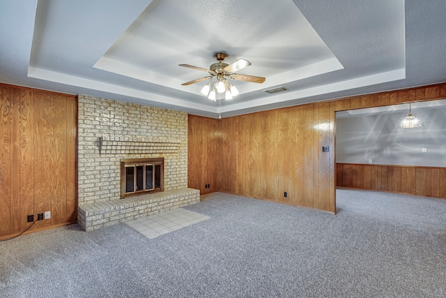 unfurnished living room featuring a fireplace, wooden walls, a raised ceiling, and light colored carpet