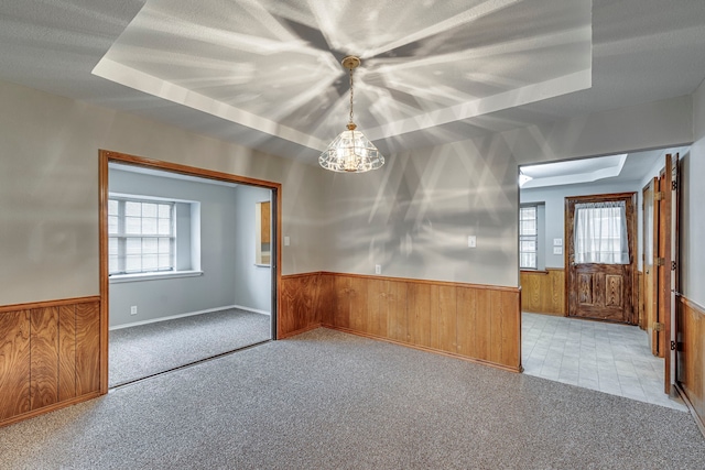 carpeted empty room featuring a raised ceiling, a textured ceiling, and wood walls