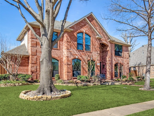 view of front of house with roof with shingles, a front lawn, and brick siding