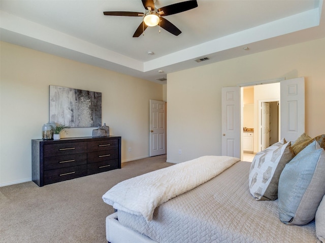 bedroom with a raised ceiling, light colored carpet, visible vents, ensuite bath, and baseboards