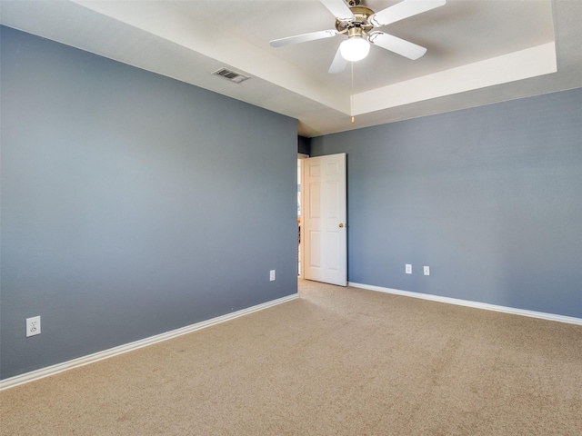 carpeted spare room featuring a ceiling fan, a raised ceiling, visible vents, and baseboards