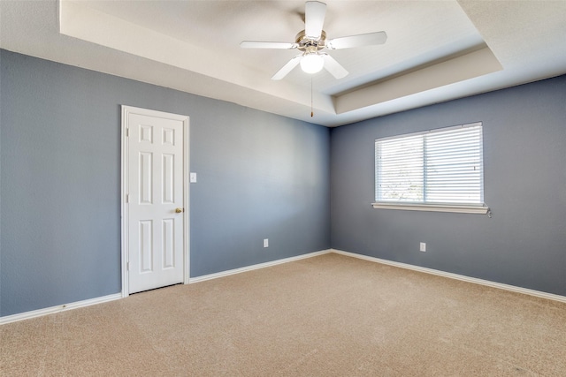 carpeted empty room with baseboards, a tray ceiling, and a ceiling fan