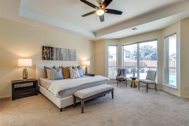 bedroom featuring light carpet, a ceiling fan, visible vents, baseboards, and a tray ceiling