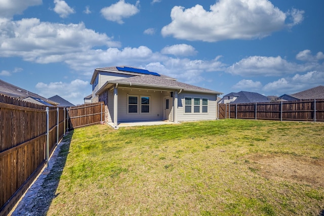 rear view of property featuring a lawn, solar panels, a fenced backyard, and a patio