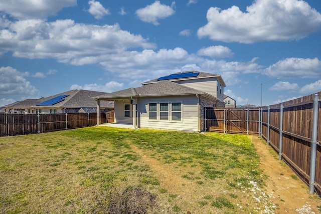 rear view of house featuring a patio, a gate, solar panels, a yard, and a fenced backyard