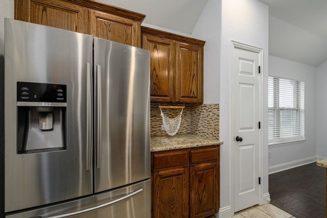 kitchen featuring stainless steel refrigerator with ice dispenser, lofted ceiling, light stone countertops, and backsplash