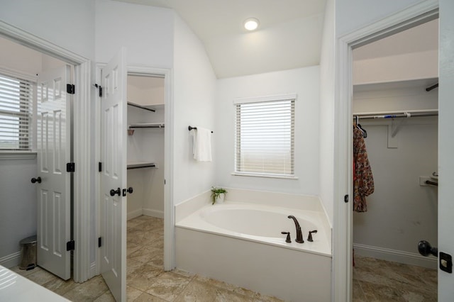 bathroom with a wealth of natural light, lofted ceiling, and a bath