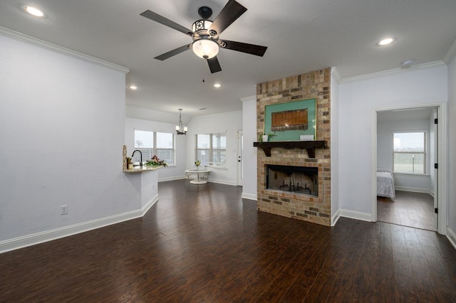 unfurnished living room featuring dark hardwood / wood-style flooring, crown molding, a fireplace, and ceiling fan with notable chandelier