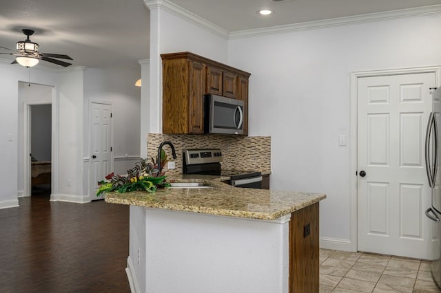 kitchen with sink, tasteful backsplash, appliances with stainless steel finishes, kitchen peninsula, and light stone countertops