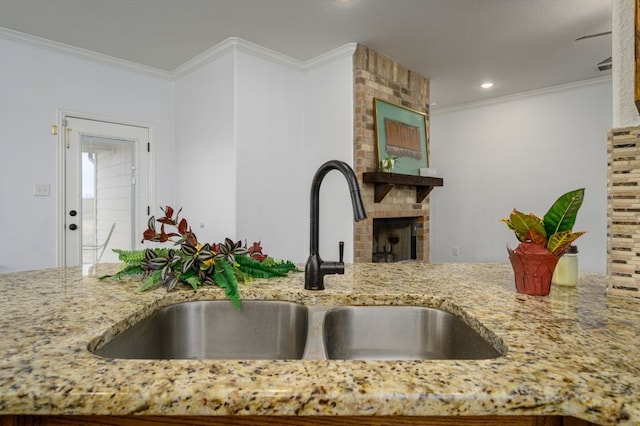 kitchen featuring crown molding, light stone counters, sink, and a brick fireplace