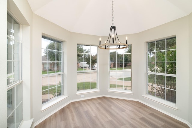 unfurnished dining area with an inviting chandelier, lofted ceiling, and hardwood / wood-style floors