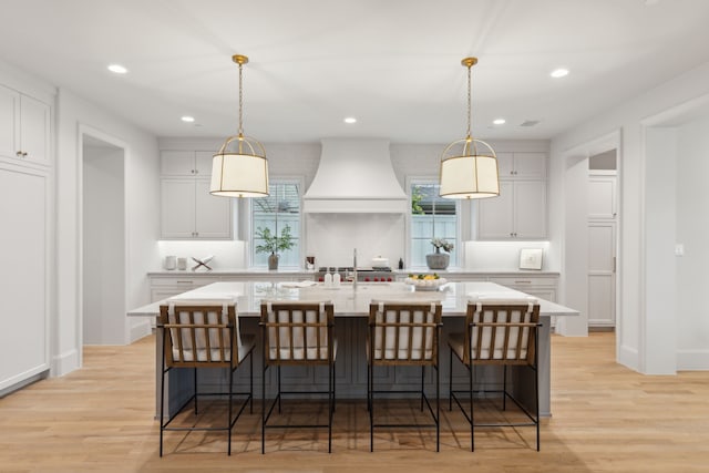 kitchen with hanging light fixtures, a kitchen breakfast bar, custom range hood, and a spacious island