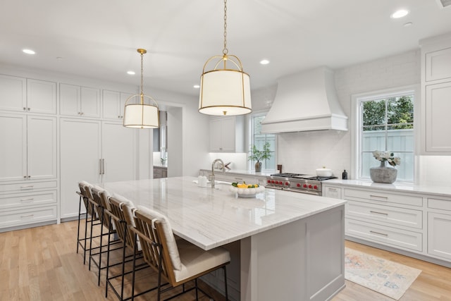 kitchen featuring custom exhaust hood, white cabinetry, a large island with sink, and range with two ovens