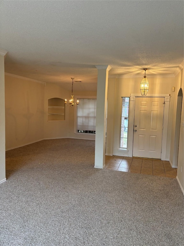 entrance foyer with an inviting chandelier, crown molding, a textured ceiling, carpet flooring, and decorative columns