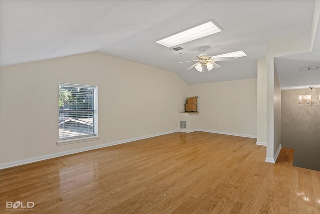 unfurnished living room with ceiling fan with notable chandelier, vaulted ceiling with skylight, and light wood-type flooring