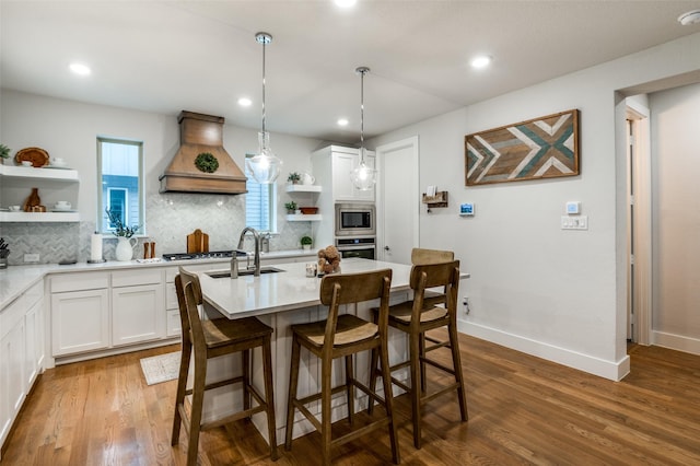 kitchen featuring white cabinetry, stainless steel appliances, custom exhaust hood, and a center island with sink