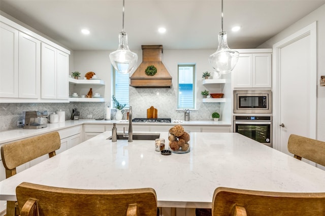 kitchen with premium range hood, white cabinetry, appliances with stainless steel finishes, and a kitchen island with sink