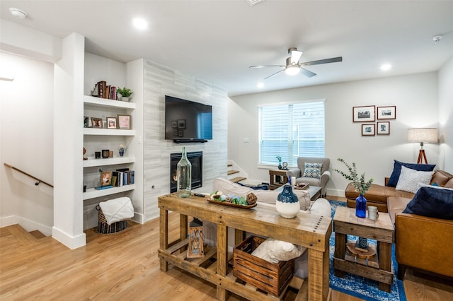 living room featuring ceiling fan, a tile fireplace, light hardwood / wood-style flooring, and built in features