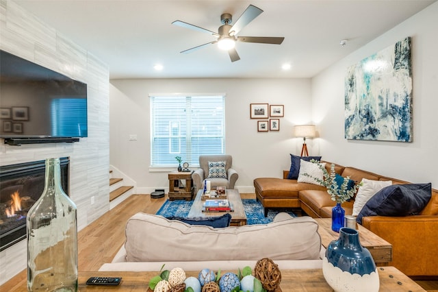 living room featuring a tiled fireplace, ceiling fan, and light hardwood / wood-style floors