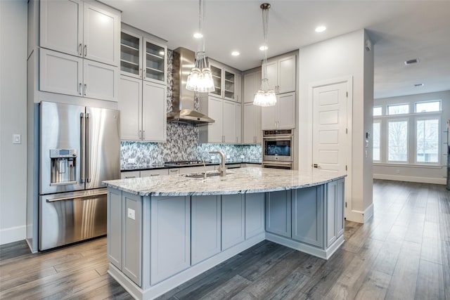 kitchen featuring appliances with stainless steel finishes, sink, a kitchen island with sink, light stone countertops, and wall chimney exhaust hood