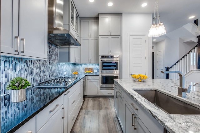 kitchen featuring sink, backsplash, stainless steel appliances, light stone countertops, and wall chimney exhaust hood