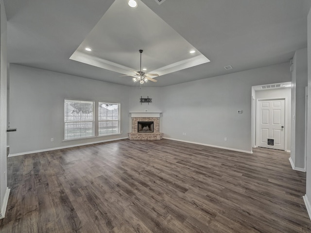 unfurnished living room featuring dark hardwood / wood-style flooring, a fireplace, a raised ceiling, and ceiling fan