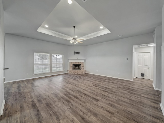 unfurnished living room featuring ceiling fan, a fireplace, a raised ceiling, and dark hardwood / wood-style flooring