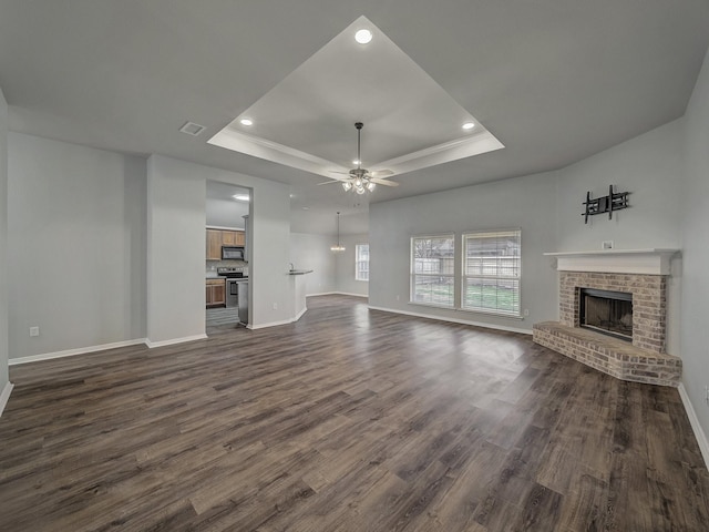 unfurnished living room with a brick fireplace, dark wood-type flooring, a raised ceiling, and ceiling fan