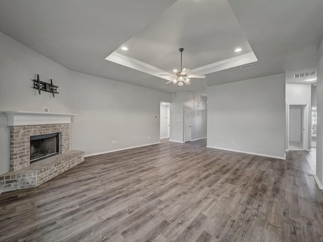 unfurnished living room with wood-type flooring, a brick fireplace, ceiling fan, and a tray ceiling