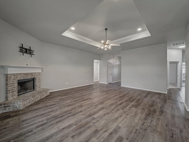 unfurnished living room featuring a tray ceiling, hardwood / wood-style floors, and a brick fireplace