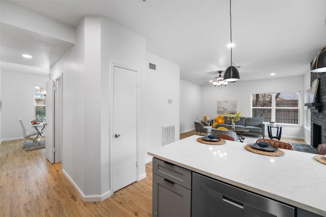 kitchen featuring pendant lighting, light hardwood / wood-style flooring, gray cabinets, a fireplace, and light stone countertops