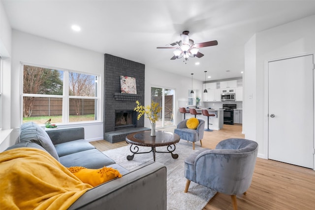 living room featuring ceiling fan, a fireplace, and light wood-type flooring