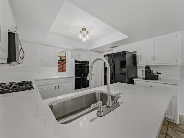 kitchen with black appliances, sink, white cabinets, a tray ceiling, and light stone countertops