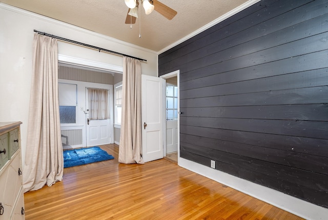 unfurnished room with a textured ceiling, light wood-type flooring, ornamental molding, wooden walls, and ceiling fan