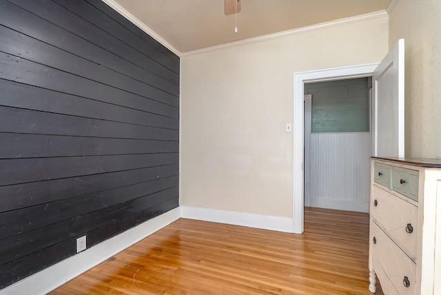 empty room featuring crown molding, wooden walls, ceiling fan, and light wood-type flooring