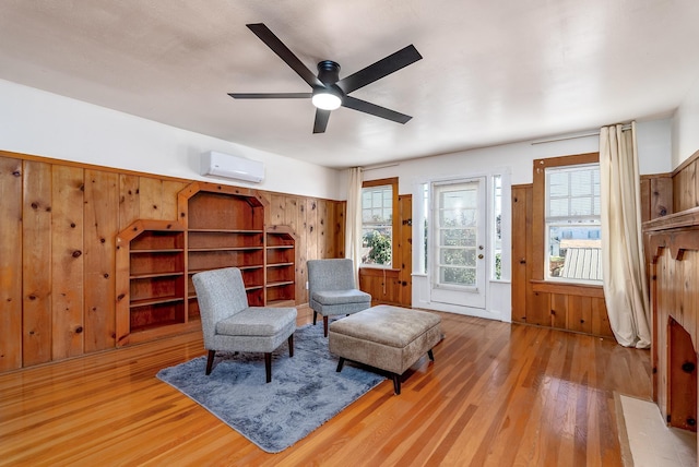 sitting room featuring ceiling fan, a wall mounted air conditioner, wooden walls, and wood-type flooring