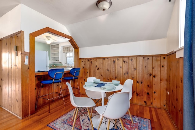 dining space with lofted ceiling, wooden walls, and light hardwood / wood-style floors