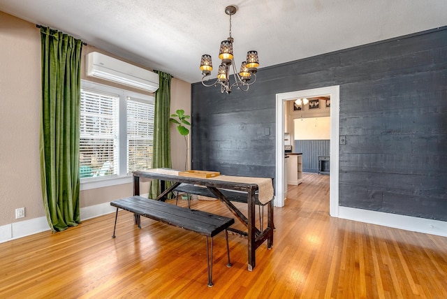 dining space with an inviting chandelier, hardwood / wood-style floors, a textured ceiling, and an AC wall unit