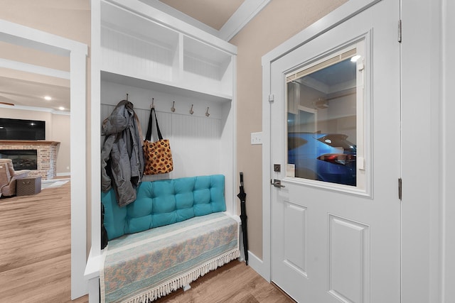 mudroom featuring crown molding, a brick fireplace, and light wood-type flooring