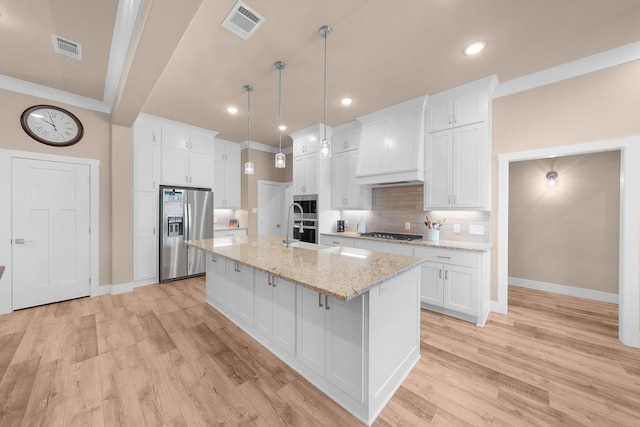 kitchen featuring appliances with stainless steel finishes, white cabinets, hanging light fixtures, a kitchen island with sink, and custom range hood