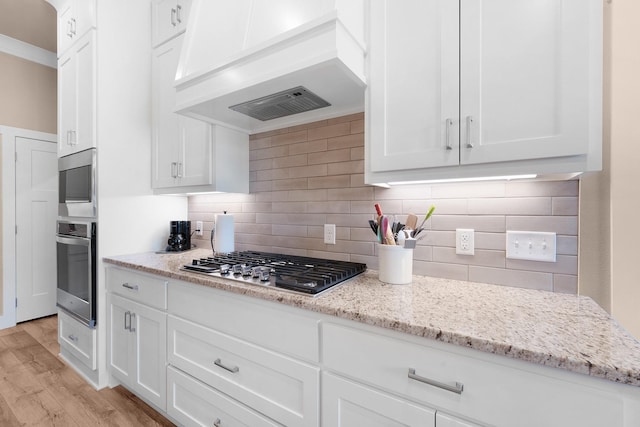 kitchen featuring tasteful backsplash, light stone counters, custom exhaust hood, and white cabinets