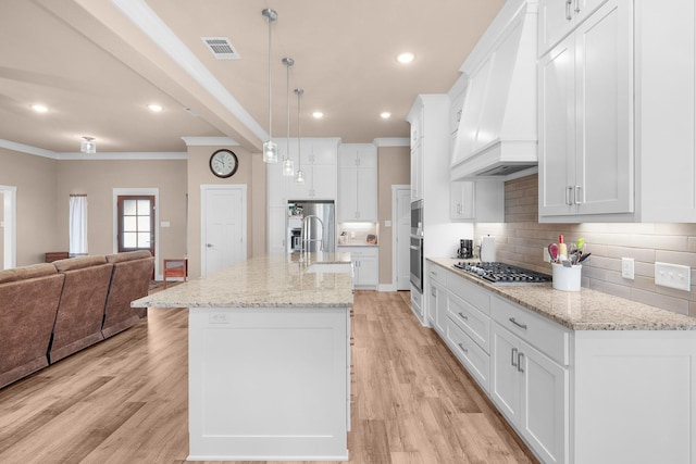 kitchen with premium range hood, white cabinetry, stainless steel appliances, a center island with sink, and decorative light fixtures