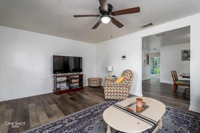 living room featuring dark hardwood / wood-style flooring, ceiling fan, and a textured ceiling