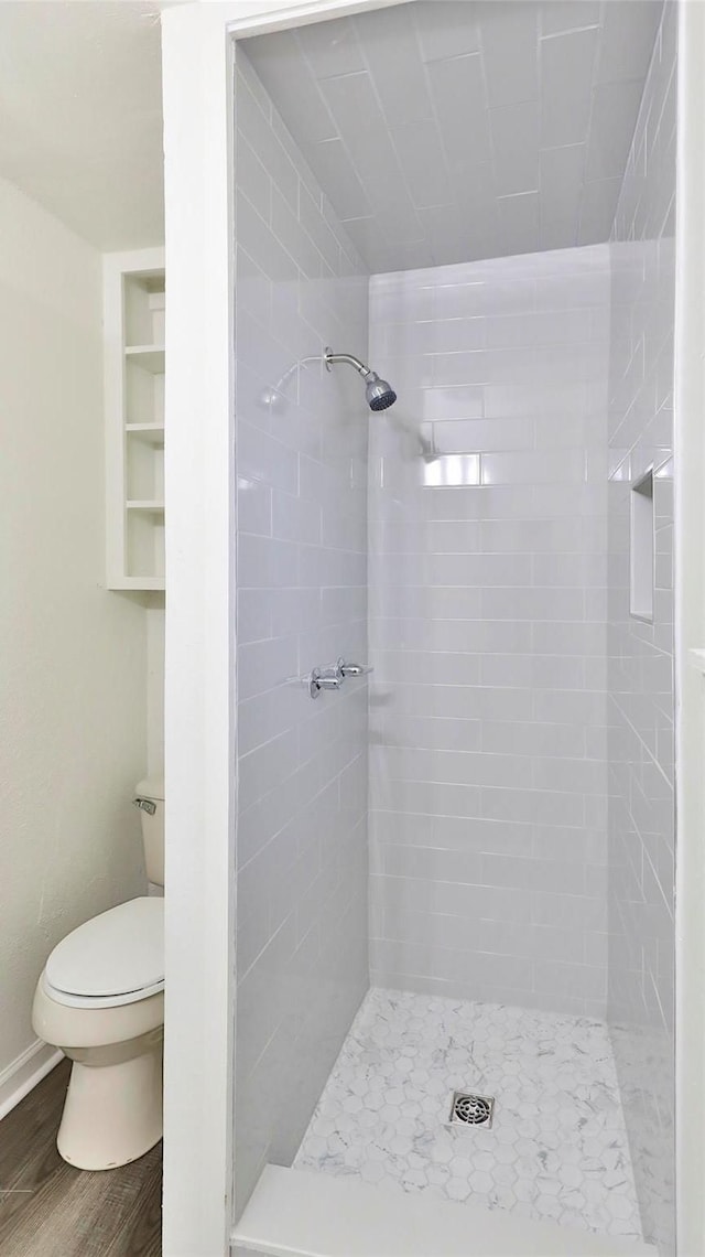 bathroom with hardwood / wood-style flooring, tiled shower, and toilet