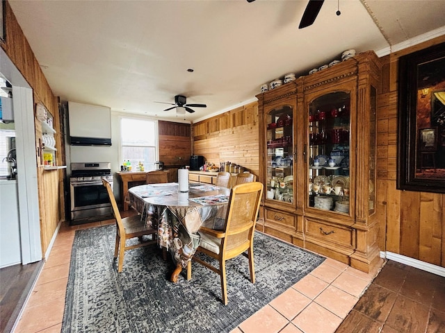 dining space with light tile patterned floors, ceiling fan, and wood walls