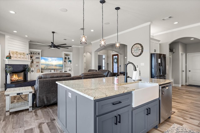 kitchen with arched walkways, a center island with sink, hanging light fixtures, freestanding refrigerator, and dishwasher